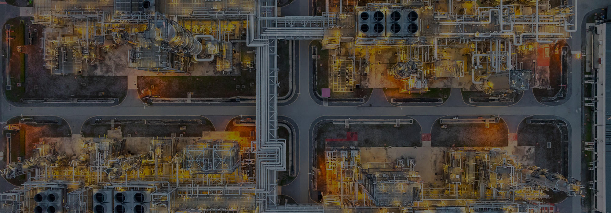 Aerial view of an industrial plant with interconnected pipes and machinery lit up at dusk.
