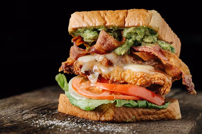 A sandwich with bacon, lettuce, tomato, and avocado on a bun.