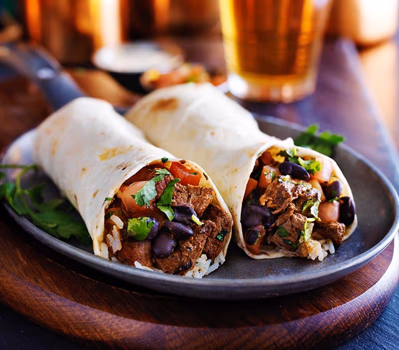 A plate of food with a burrito and a beer.