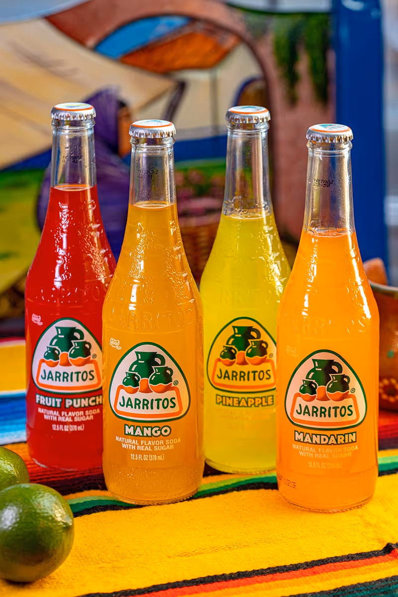 Four bottles of Jarritos soda are lined up on a table.