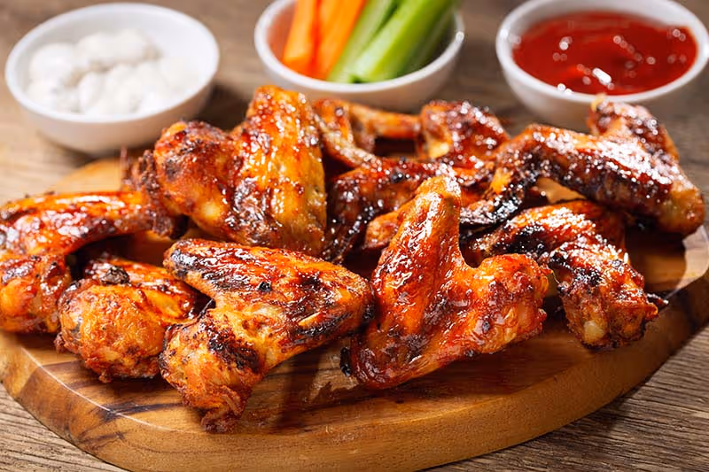 A wooden cutting board with a plate of chicken wings and carrots.