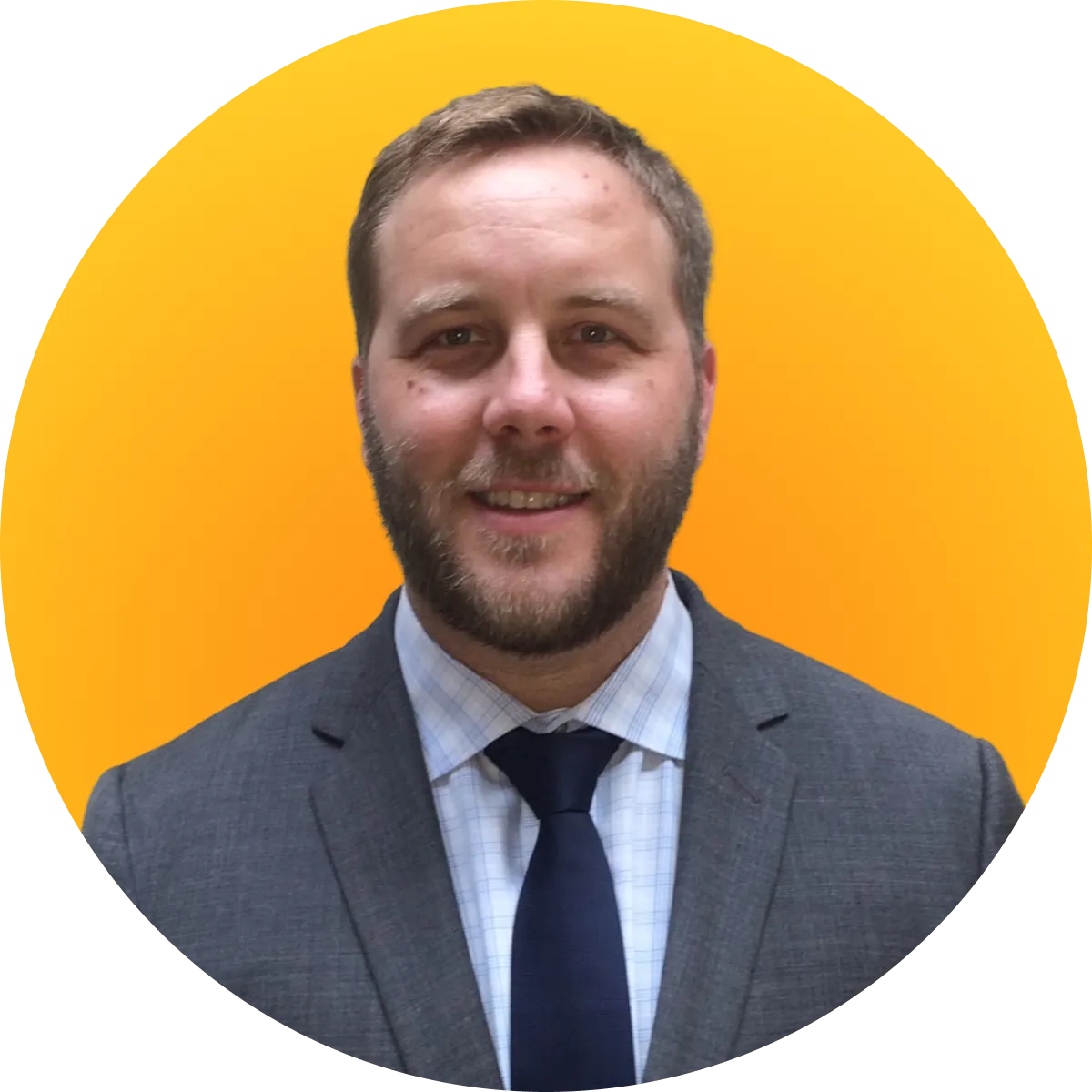 Smiling man with short hair and beard wearing a gray suit, white checkered shirt, and dark tie on yellow background.