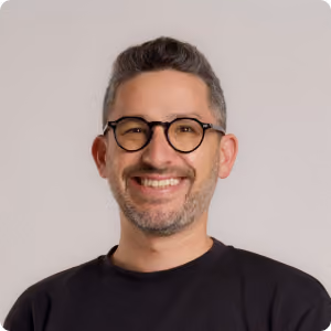 Smiling man with short gray hair and beard wearing round glasses and a black shirt.