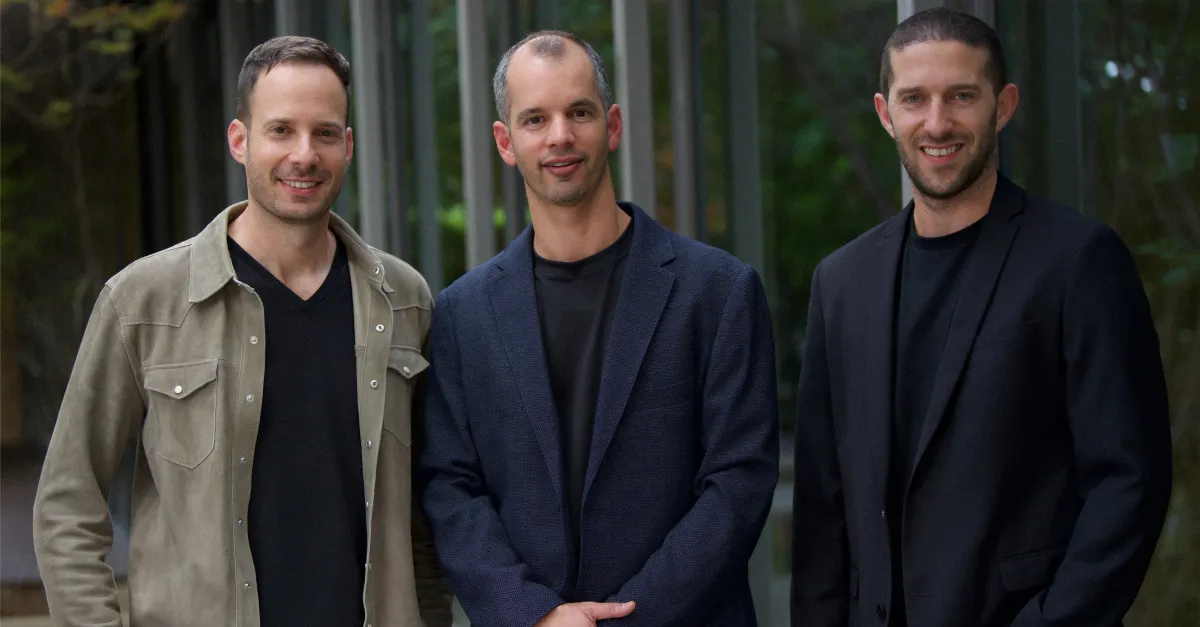 Three men standing outdoors in smart casual attire, smiling at the camera with trees in the background.