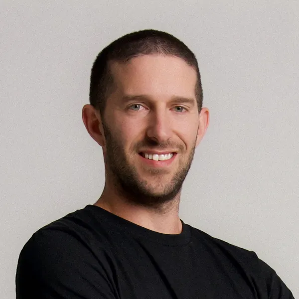 Smiling man with short dark hair and beard wearing a black shirt against a plain background.