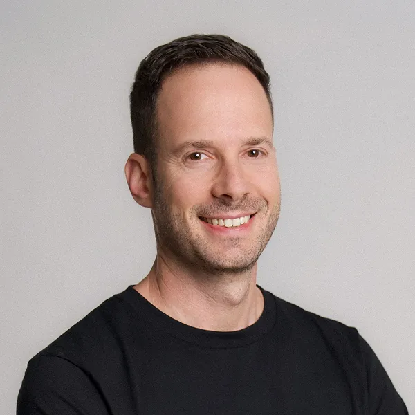 Smiling man with short dark hair wearing a black shirt against a plain light background.