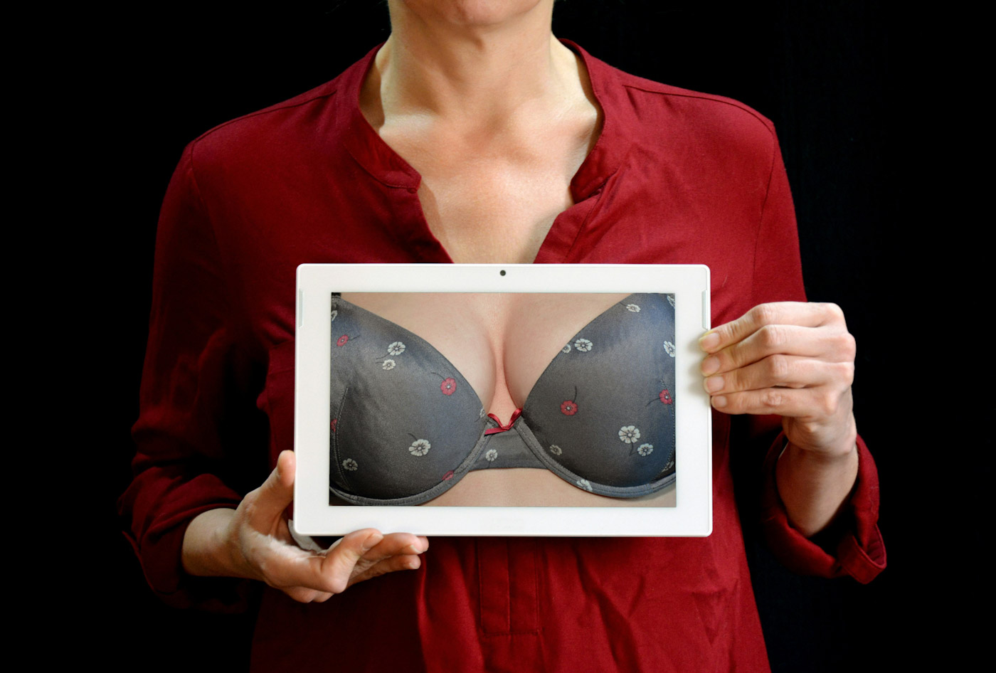 A woman holds a photo of breast cleavage in a bra over her unseen chest. Photo by Pixabay on Pexel