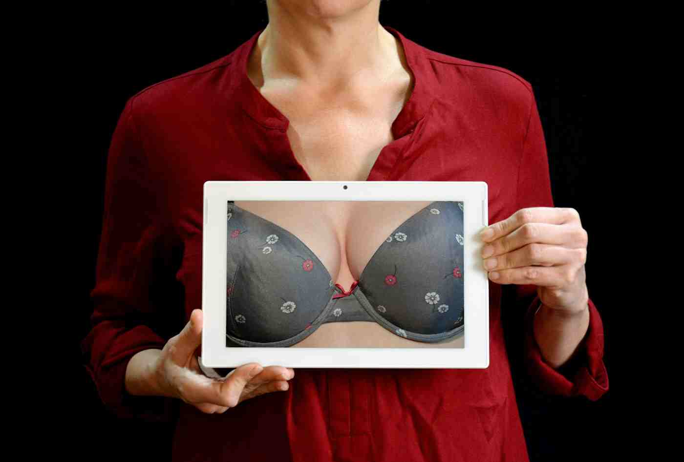 A woman holds a photo of breast cleavage in a bra over her unseen chest. Photo by Pixabay on Pexel
