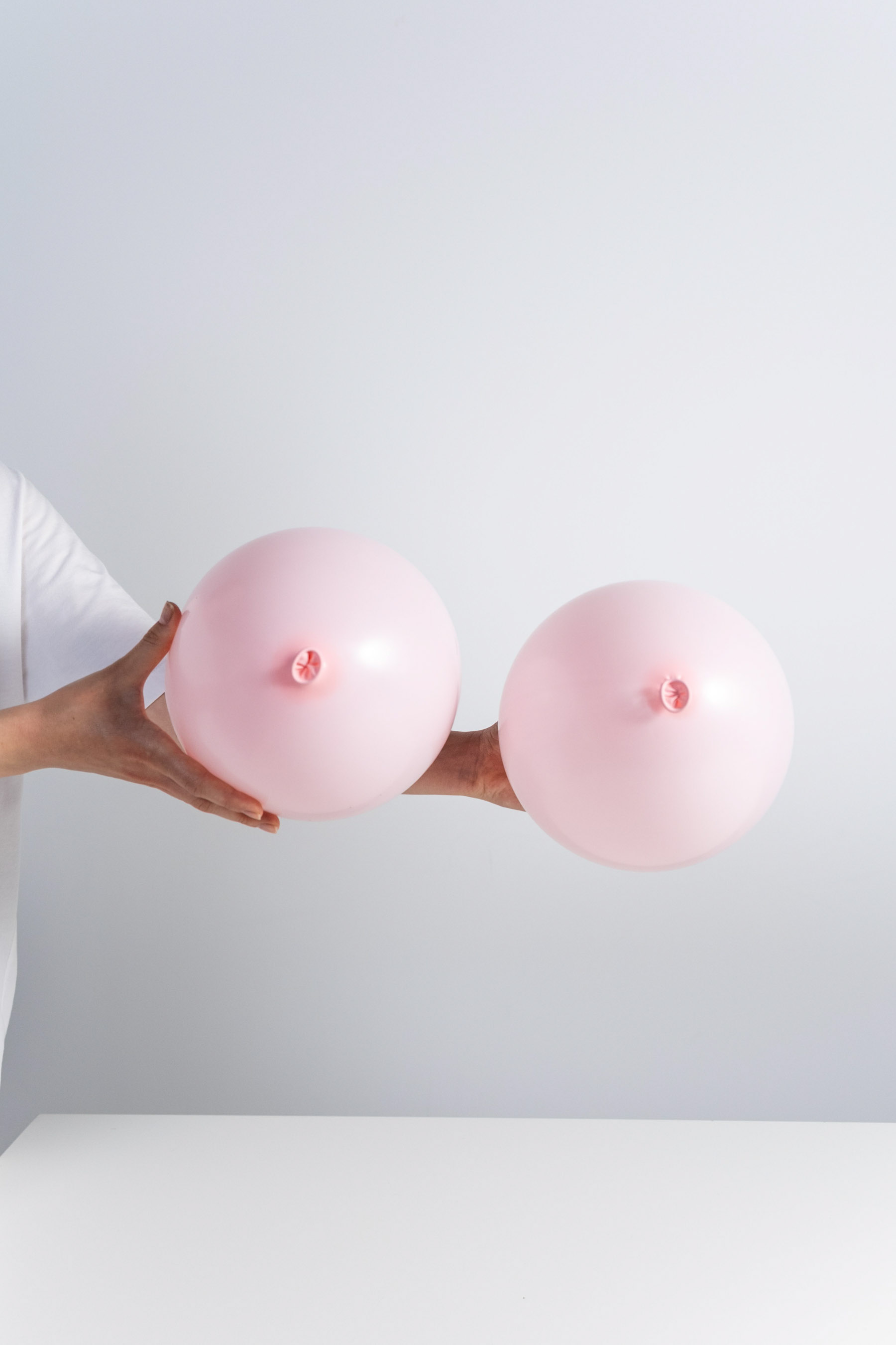 A woman holds two balloons that are staged to represent breasts on a white background