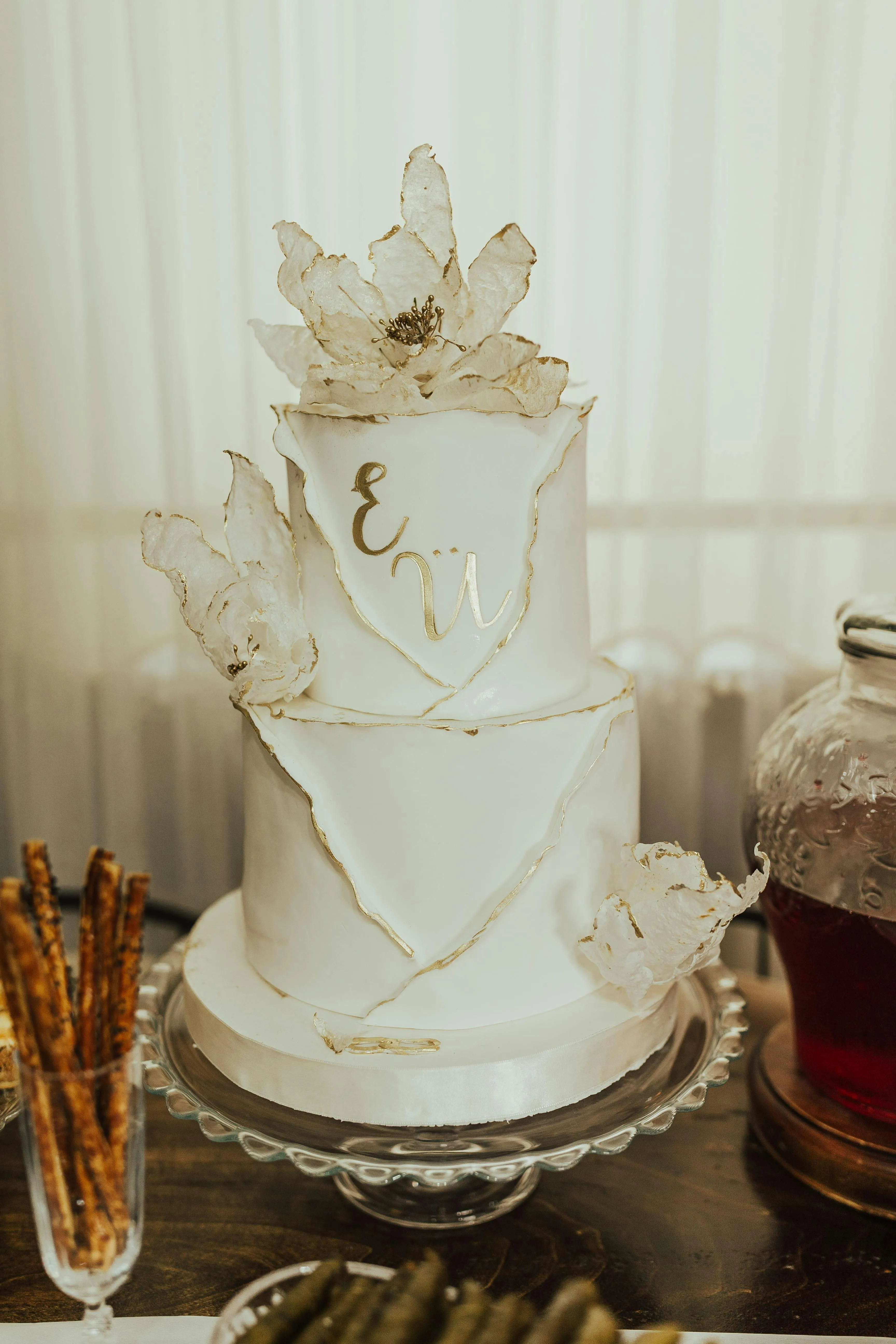 Two-tier white cake with gold-edged decorations and translucent white flowers on top and sides.