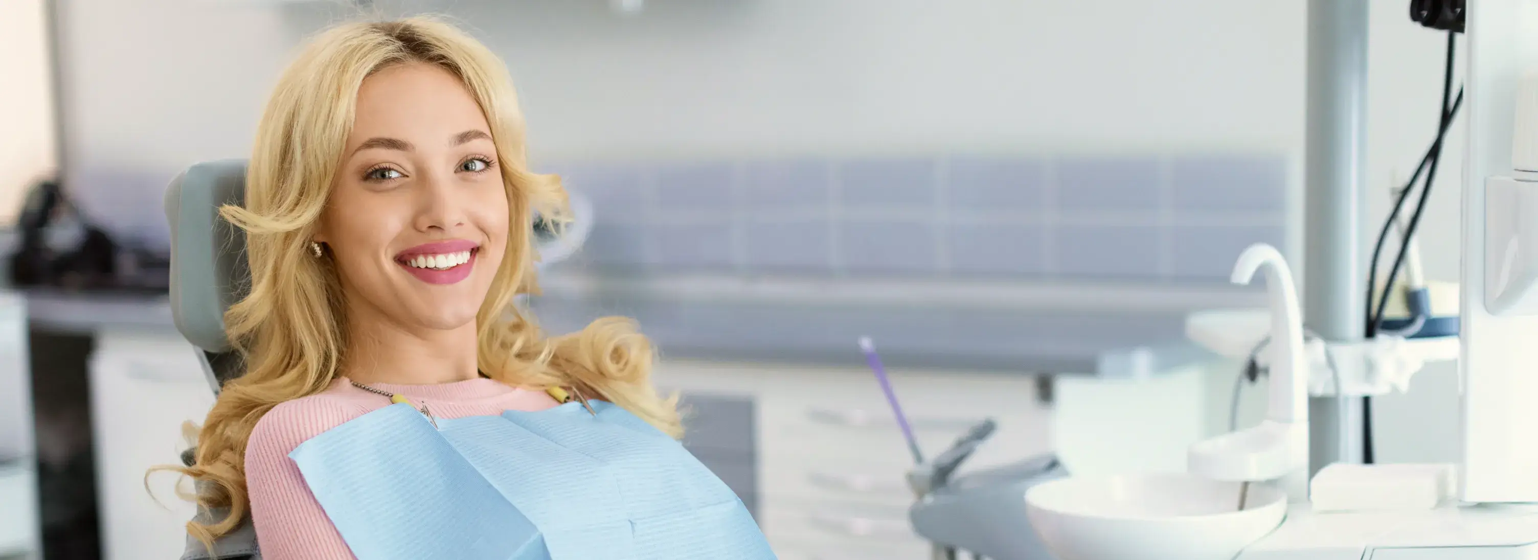 A woman sitting in a dentist chair with a toothbrush in her mouth.
