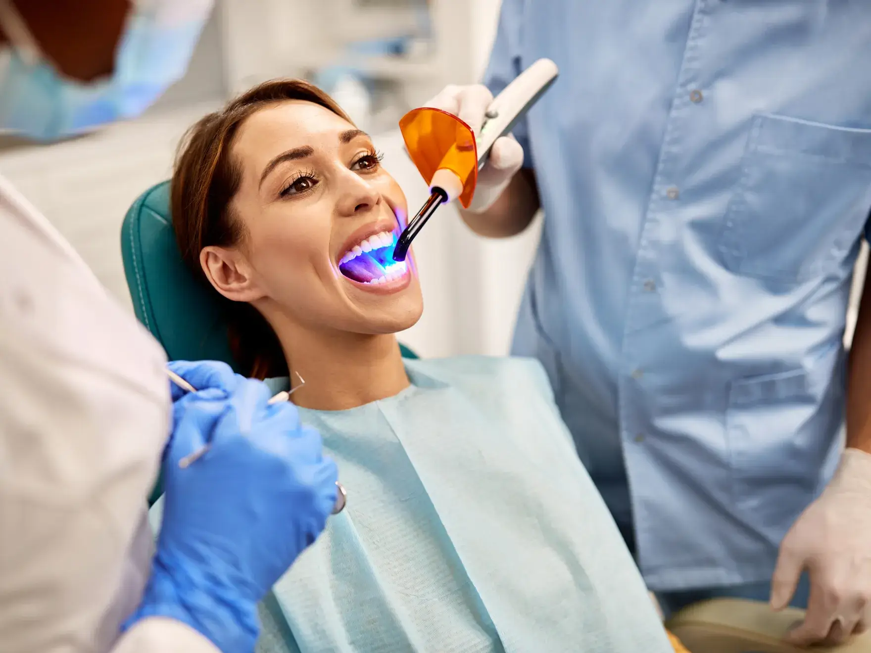 A woman sitting in a dentist chair with a toothbrush in her mouth.