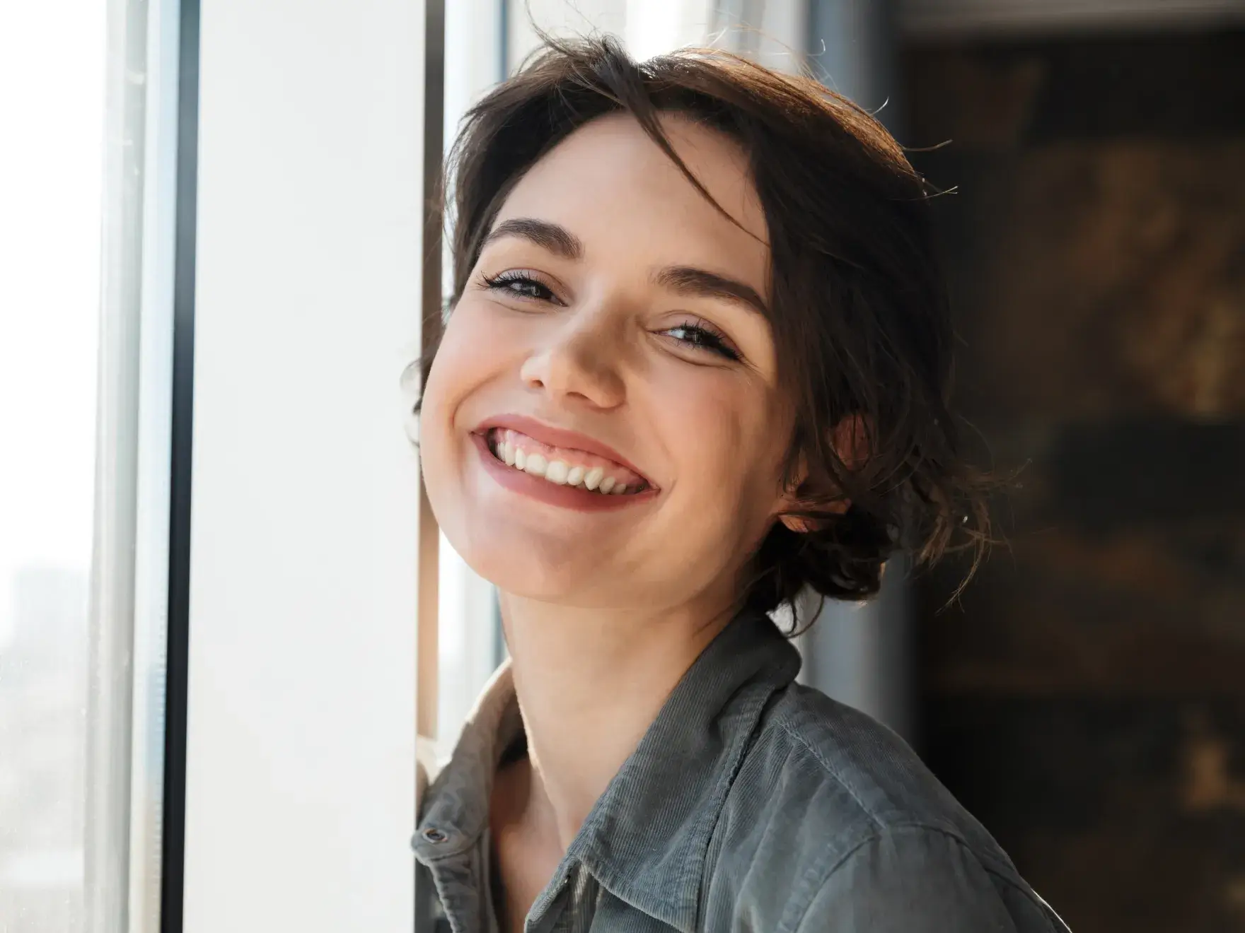 A woman smiling and leaning against a window.
