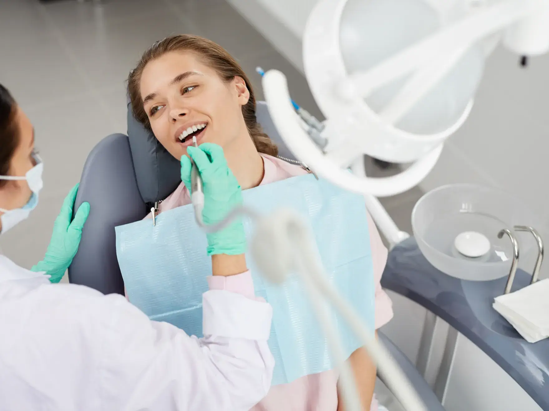 A woman sitting in a dentist chair with a toothbrush in her mouth.