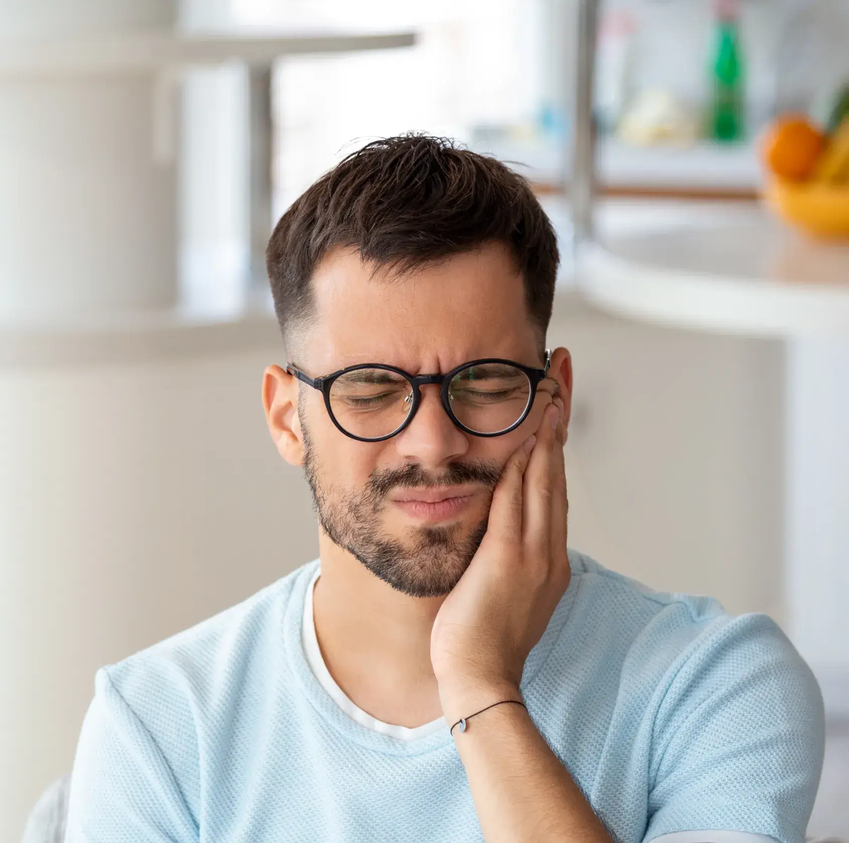 A man wearing glasses sitting down with his hand on his face.