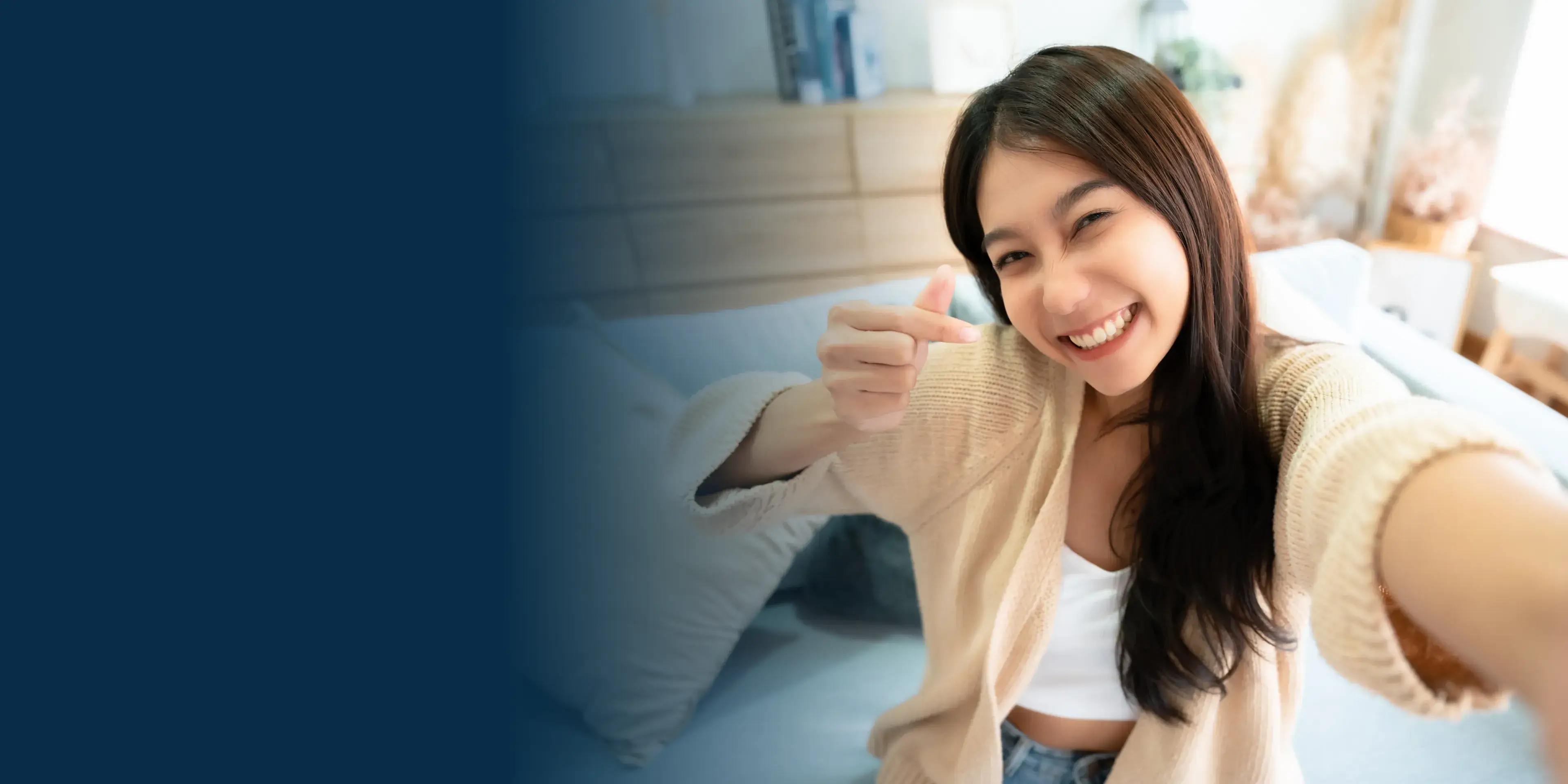A woman giving a thumbs up in front of a bed.