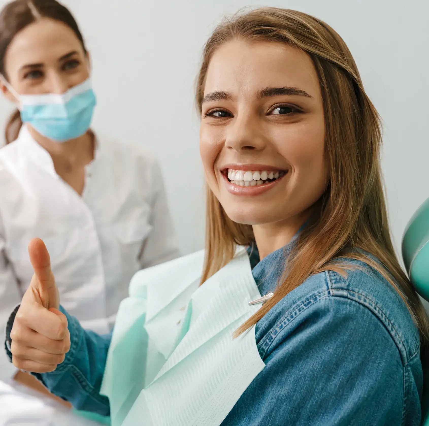 A woman in a dentist's office giving a thumbs up.
