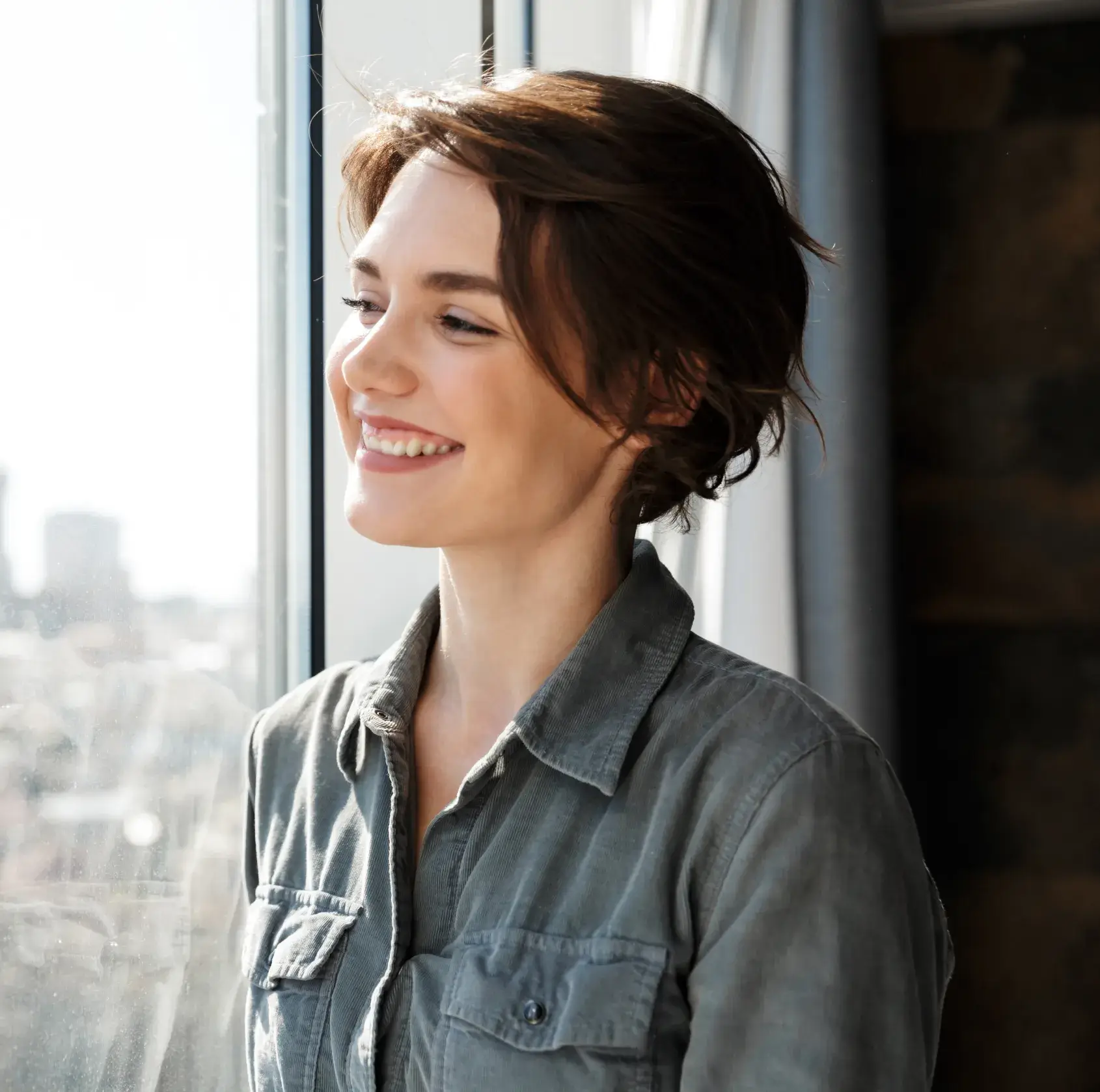 A woman standing next to a window smiling.