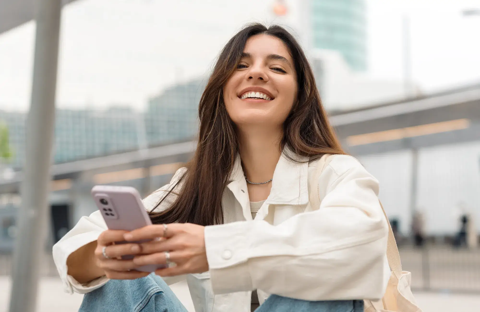 A woman sitting on the ground looking at her cell phone.