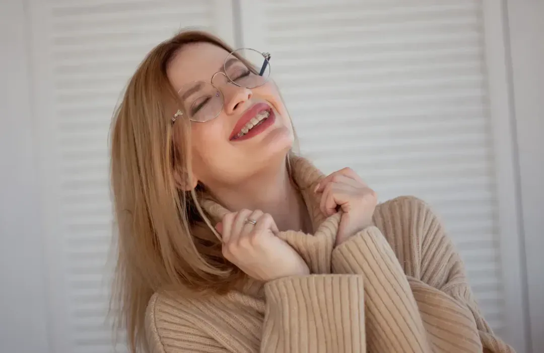 A woman wearing glasses and a sweater smiling.