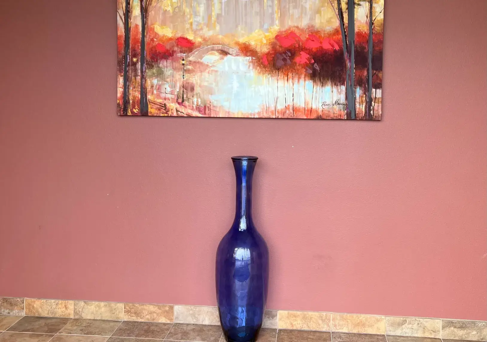 A blue vase sitting in front of a painting on a wall.