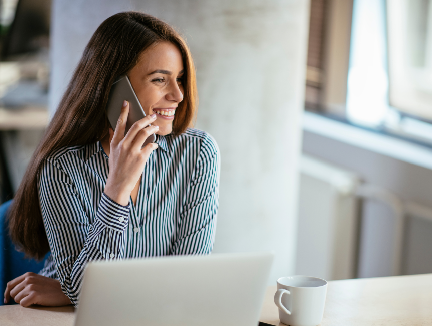 Smiling woman on mobile, sitting in front of laptop