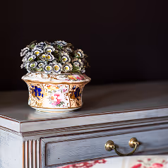 Decorative floral-patterned porcelain vase with white flowers on a gray wooden drawer with brass handles.