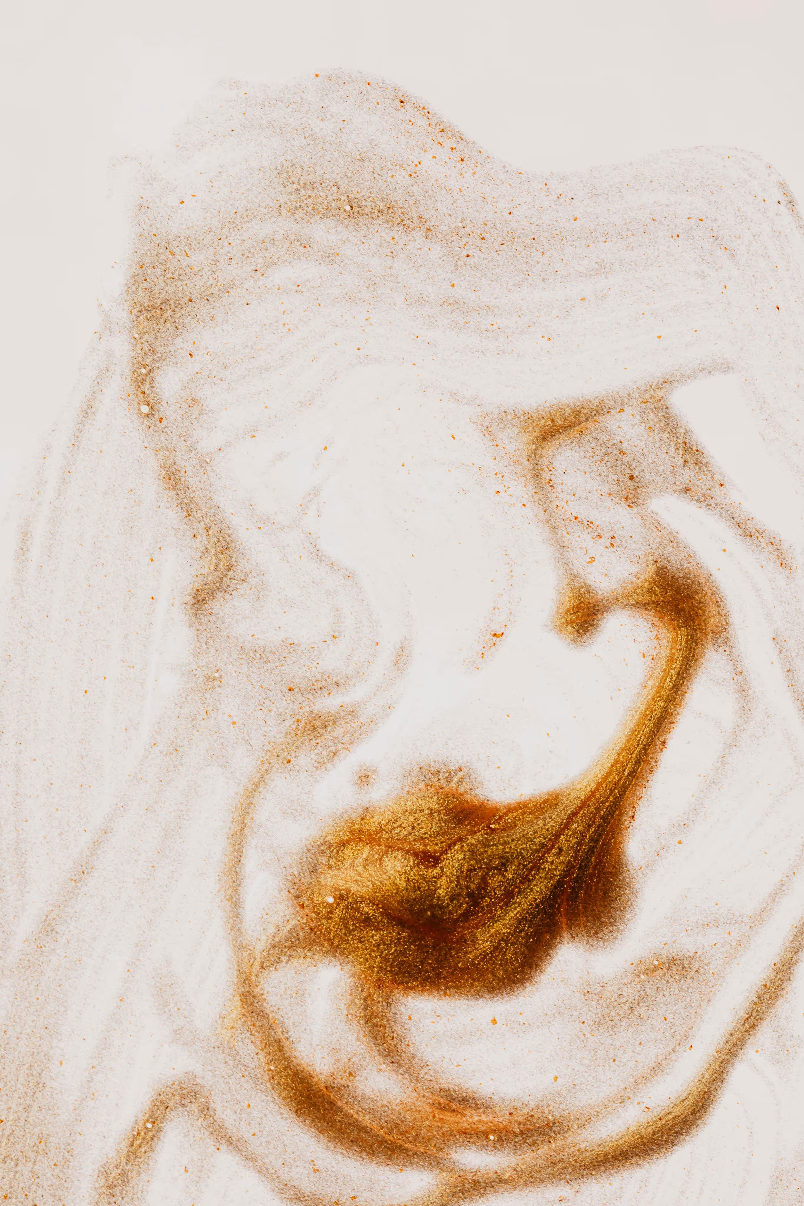 Swirling golden and brown powder particles creating an abstract pattern on a white background.