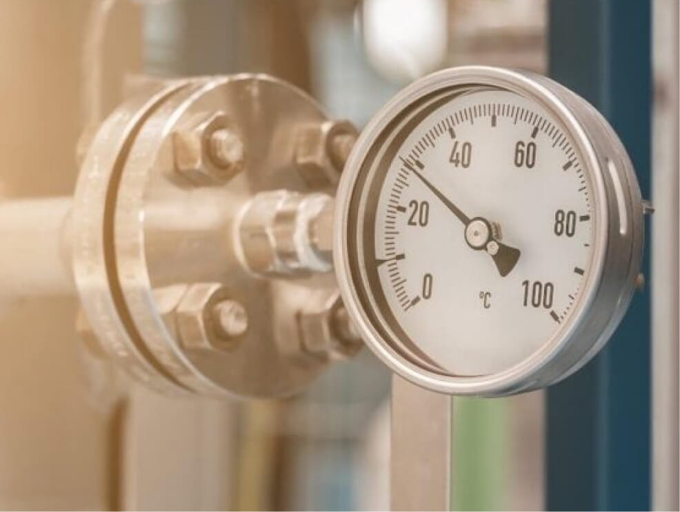 Close-up of a metal industrial thermometer showing approximately 15°C on a pipe fitting.