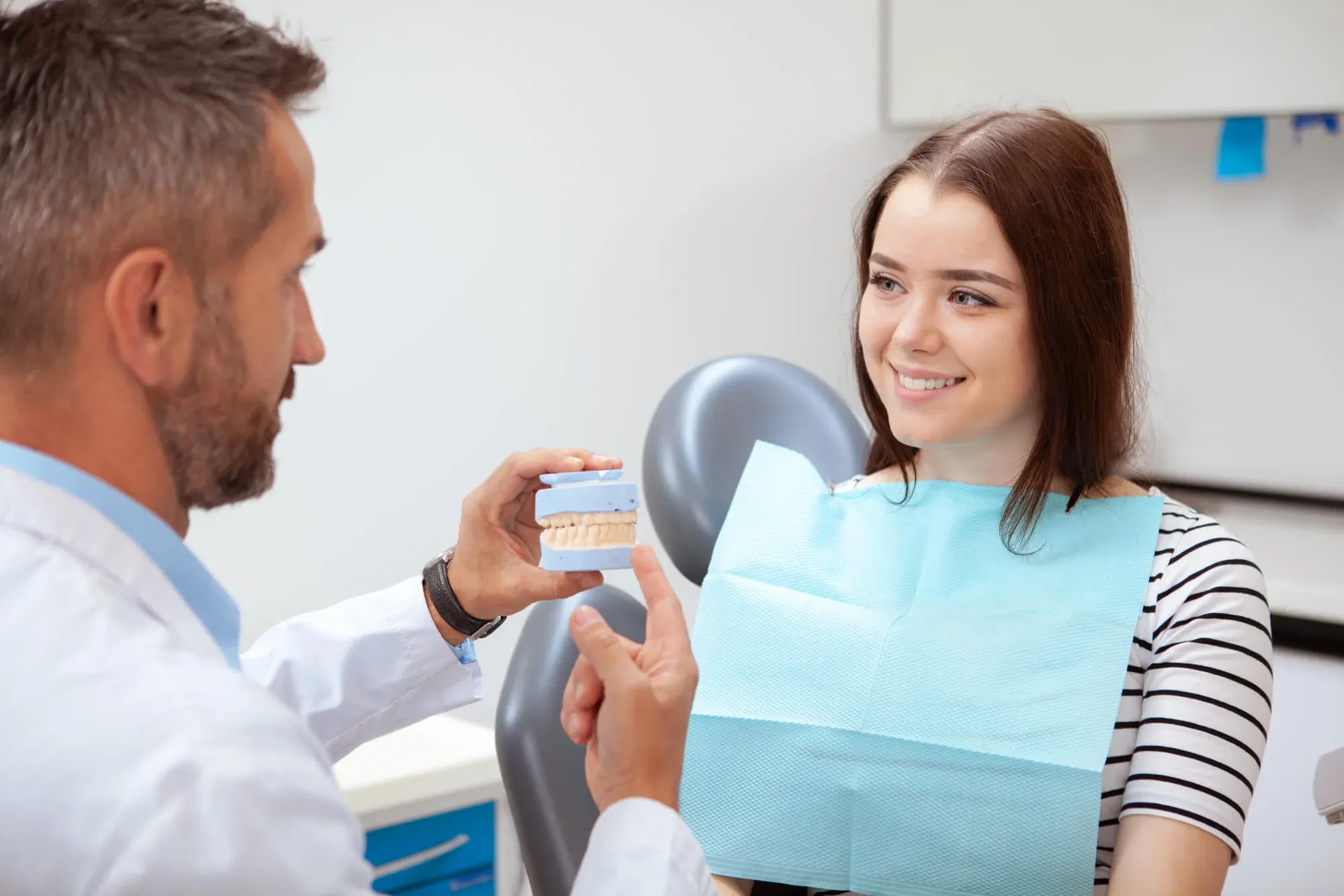 Dentist showing a tooth shade guide to a smiling woman in a modern dental clinic.