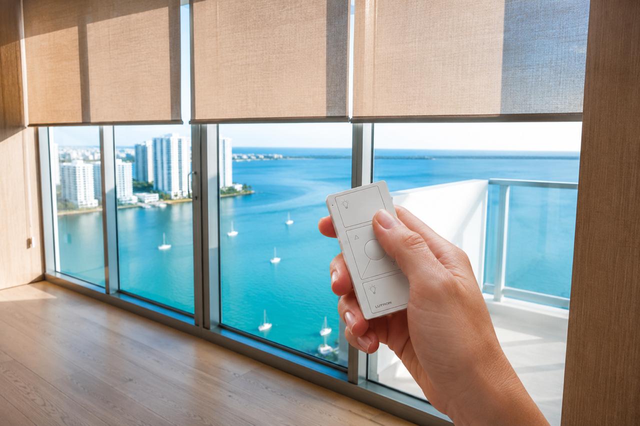 Hand using a remote to control roller shades in a Miami high-rise overlooking the bay