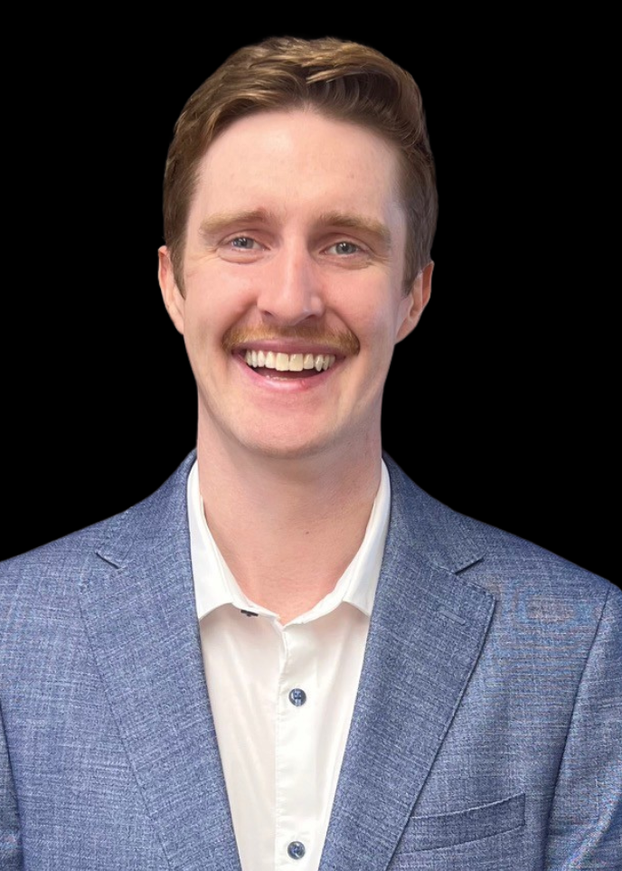 Smiling man with brown hair and mustache wearing a blue blazer and white shirt against a black background.