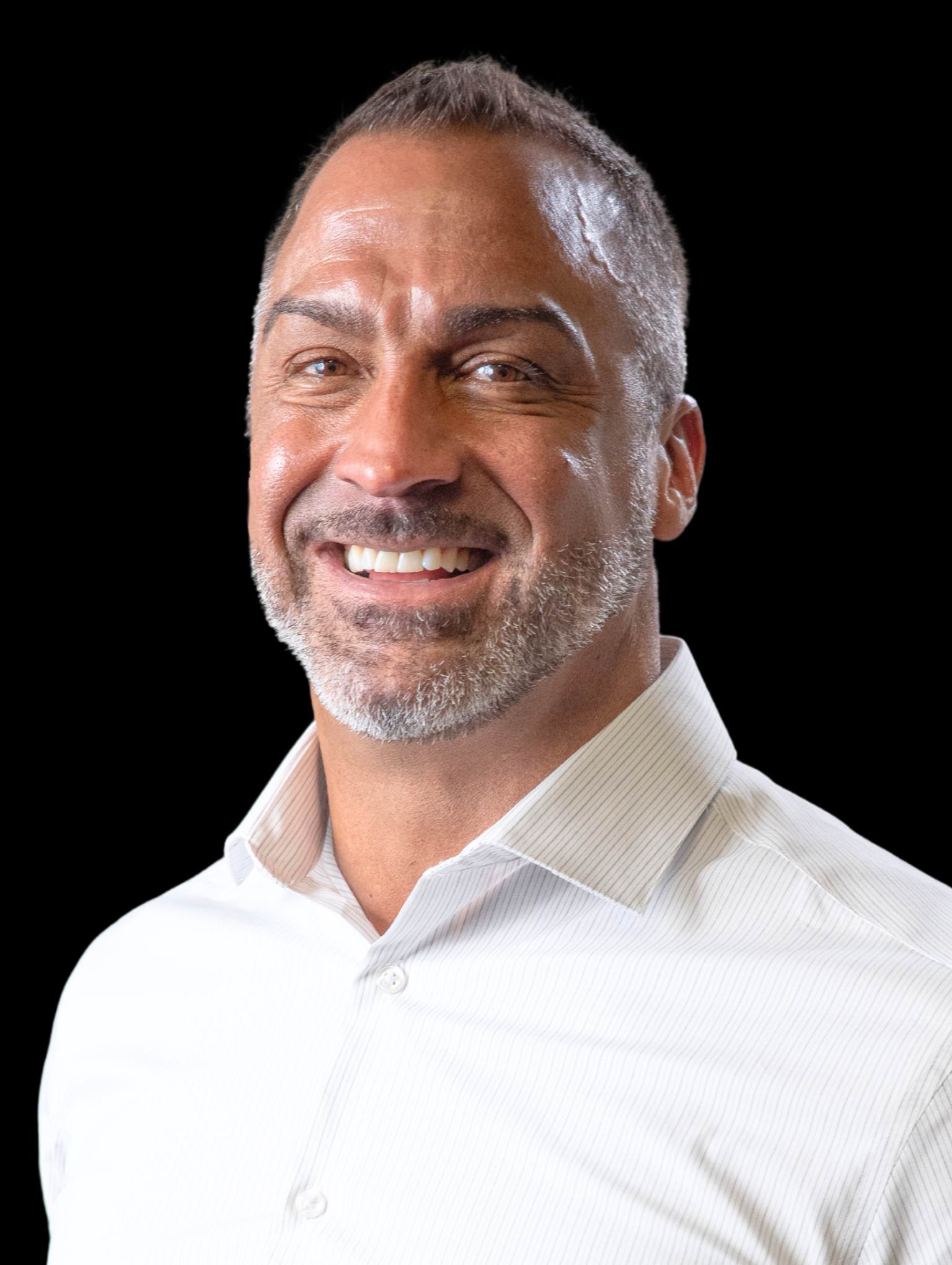 Smiling man with short black hair and beard wearing a white collared shirt against a black background.