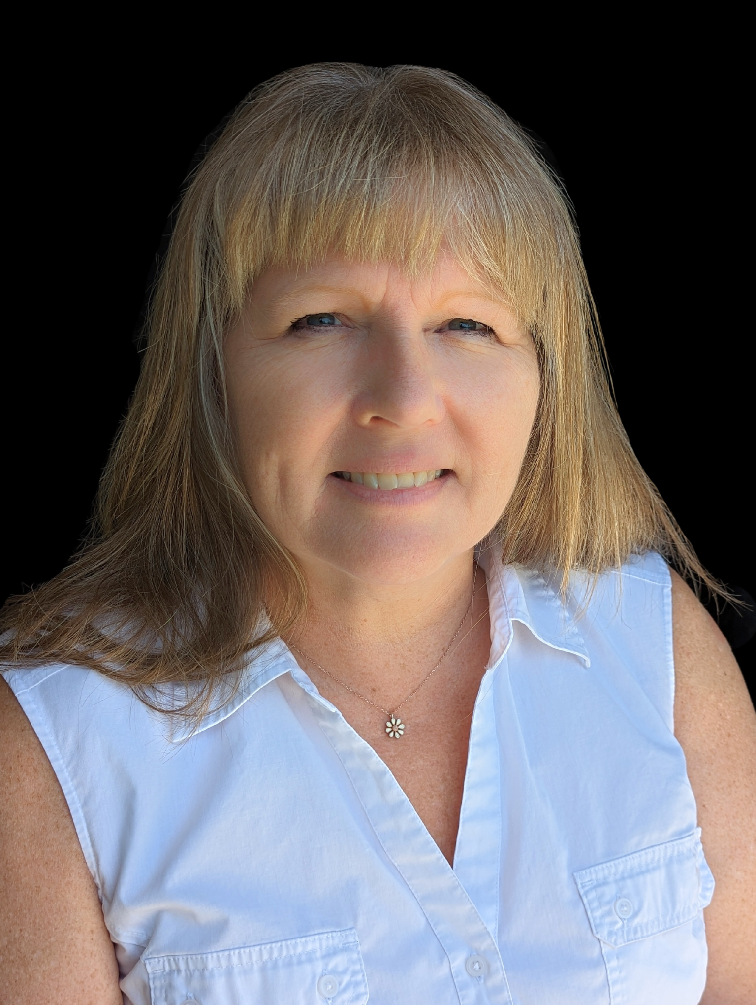 Smiling woman with light brown hair, wearing a sleeveless white shirt and a flower pendant necklace, against a black background.