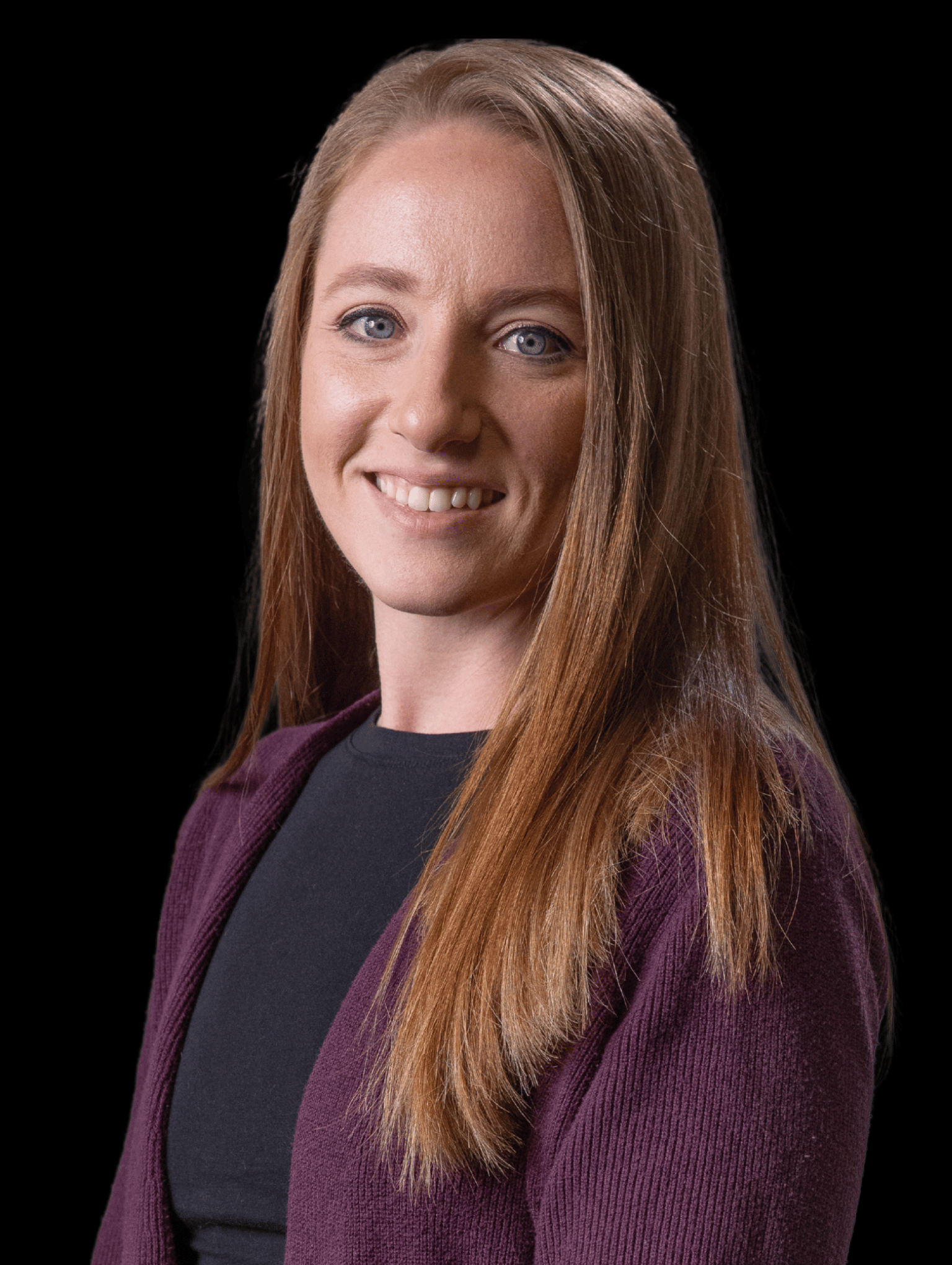 Smiling woman with long straight light brown hair, wearing a black top and a purple cardigan, against a black background.