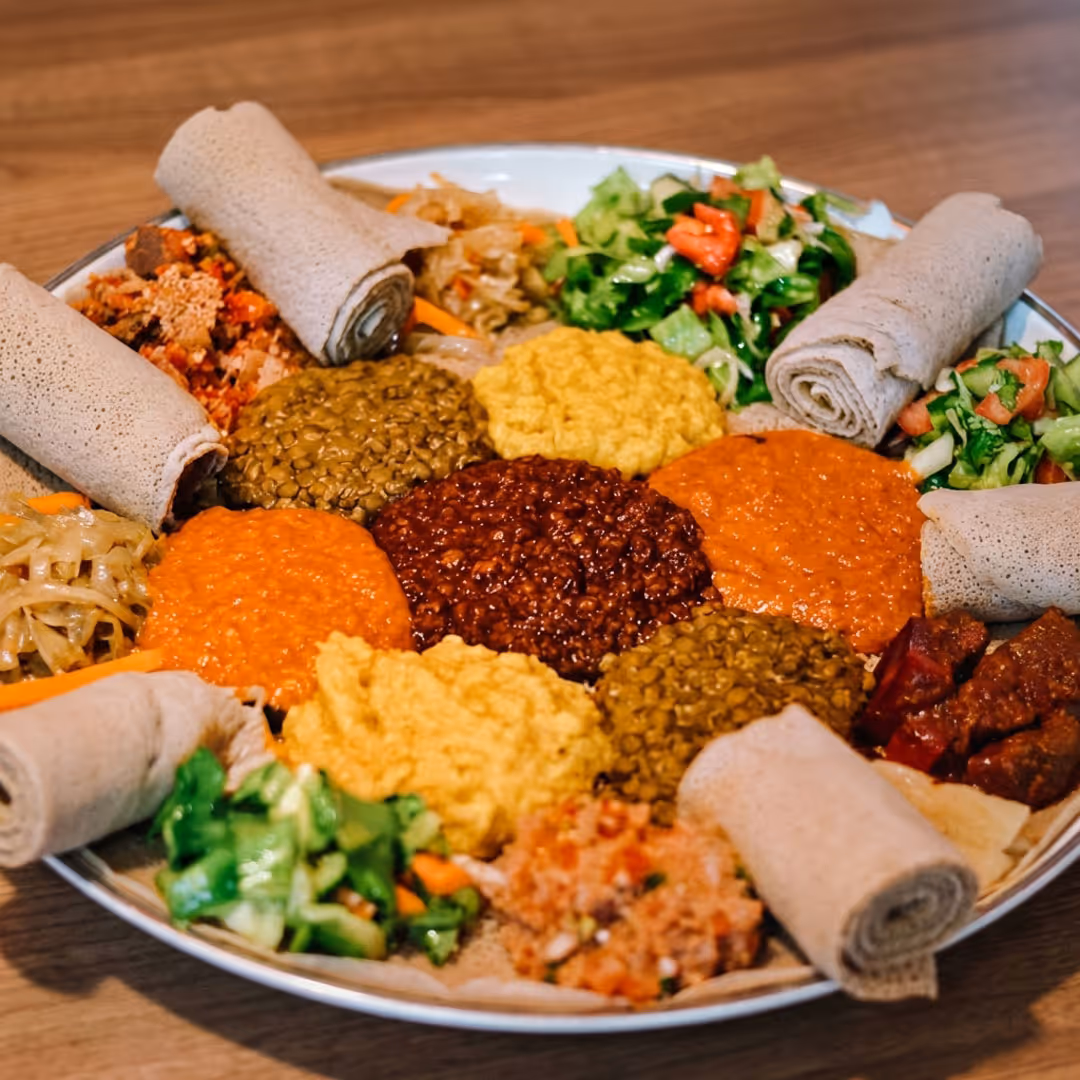 Plate of Ethiopian food featuring rolled injera bread and various lentil stews, vegetables, and salads.
