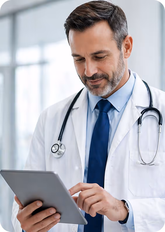 Male doctor in white coat and stethoscope using a digital tablet in a bright medical office.