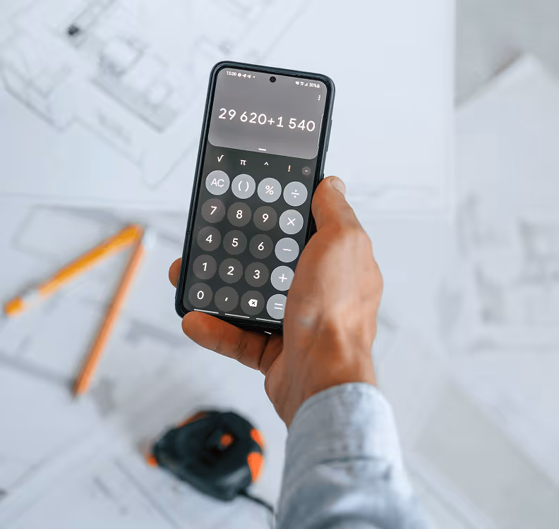 Hand hält Smartphone mit geöffnetem Taschenrechner über Bauplänen, mathematische Berechnung auf Display, orangefarbene Stifte.