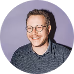 Lächelnder Mann mit Brille vor lila Hintergrund.
