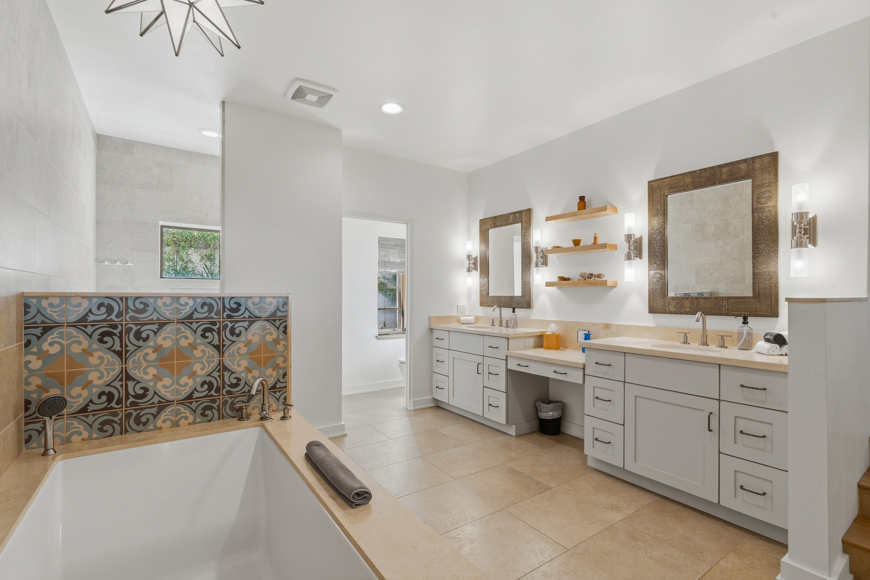 Bathroom with a patterned tile tub surround and dual vanities, shown with bright, airy photo editing.