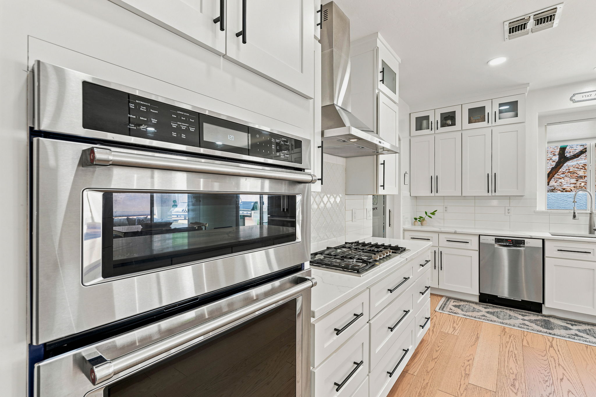 Modern white kitchen with stainless steel double ovens and a gas cooktop.