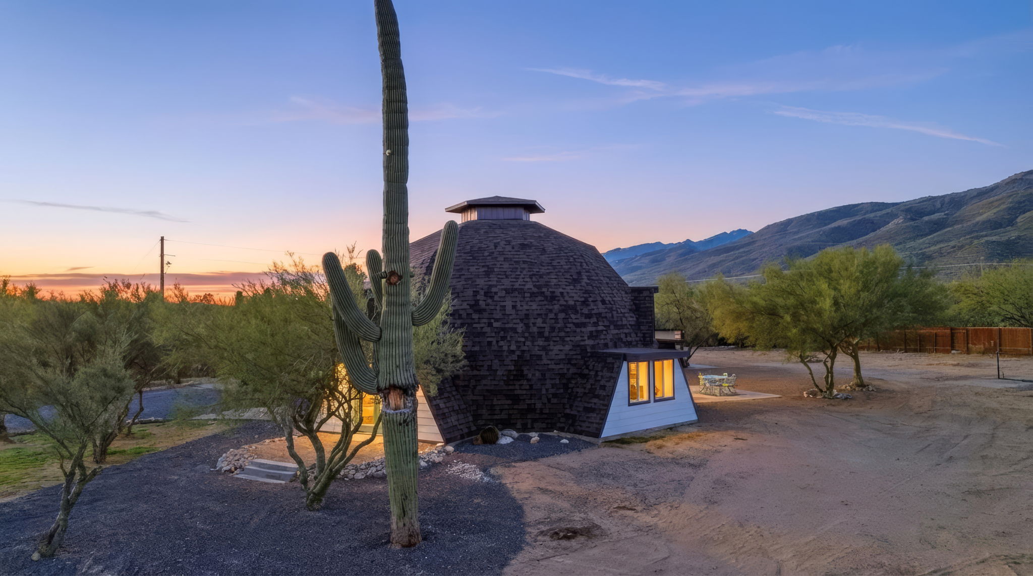 Geodesic dome house at dusk in the Sonoran Desert, with a saguaro and mountain backdrop.