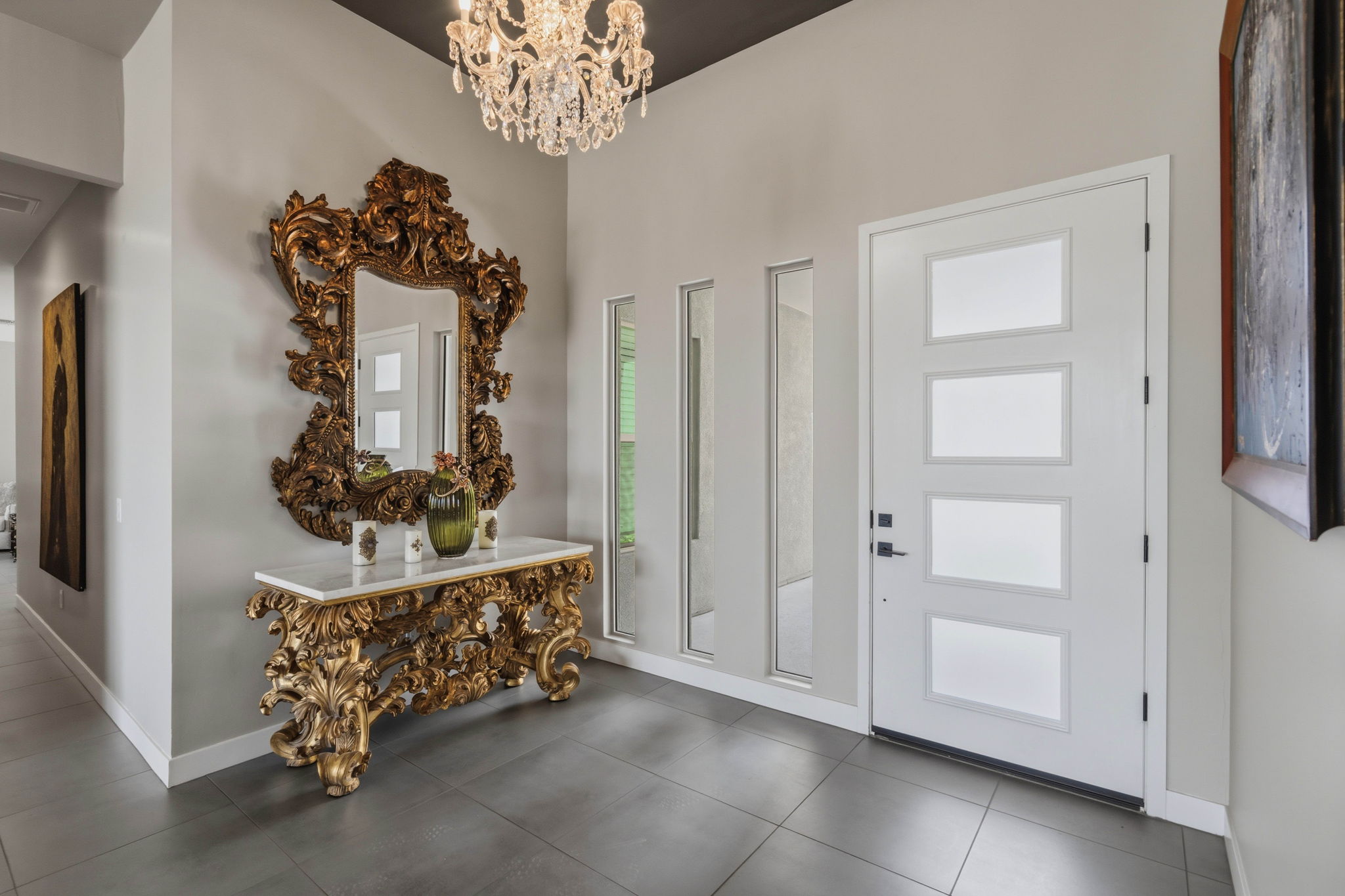 Modern home foyer with a chandelier, ornate mirror, and white front door.