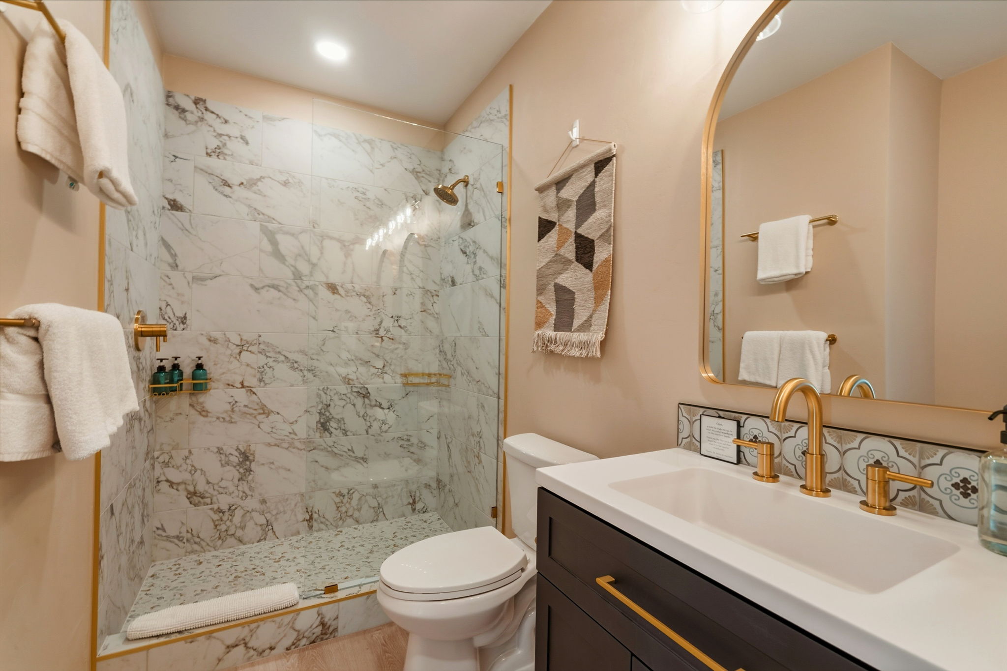Bathroom with a glass shower, gold fixtures, dark wood vanity, and gold-framed mirror.