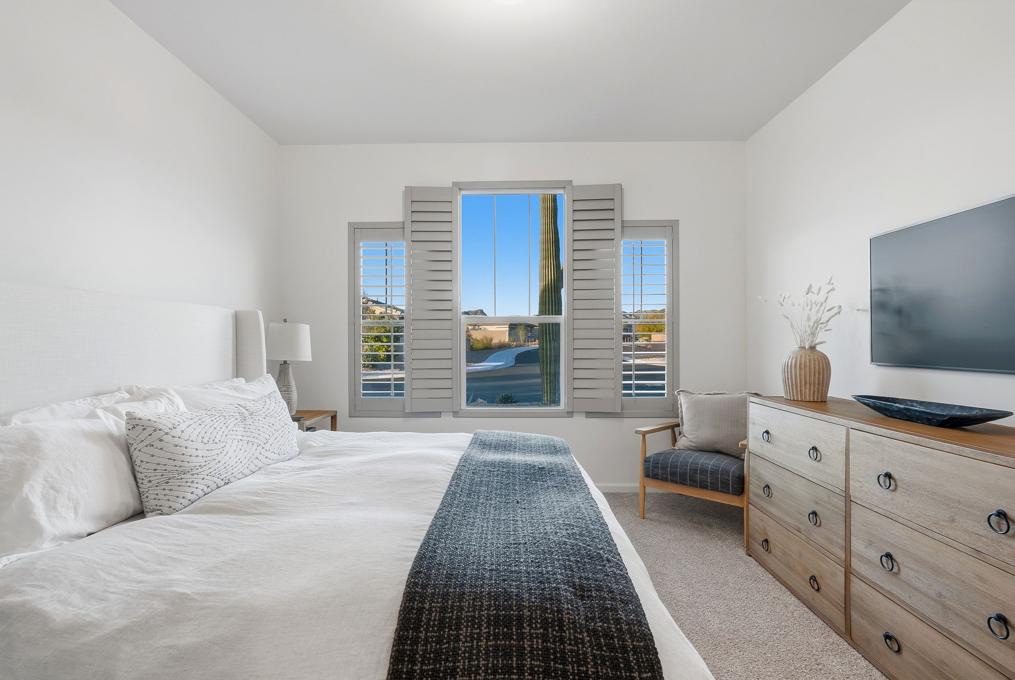 Bright modern bedroom with white bedding and a view of a saguaro cactus.