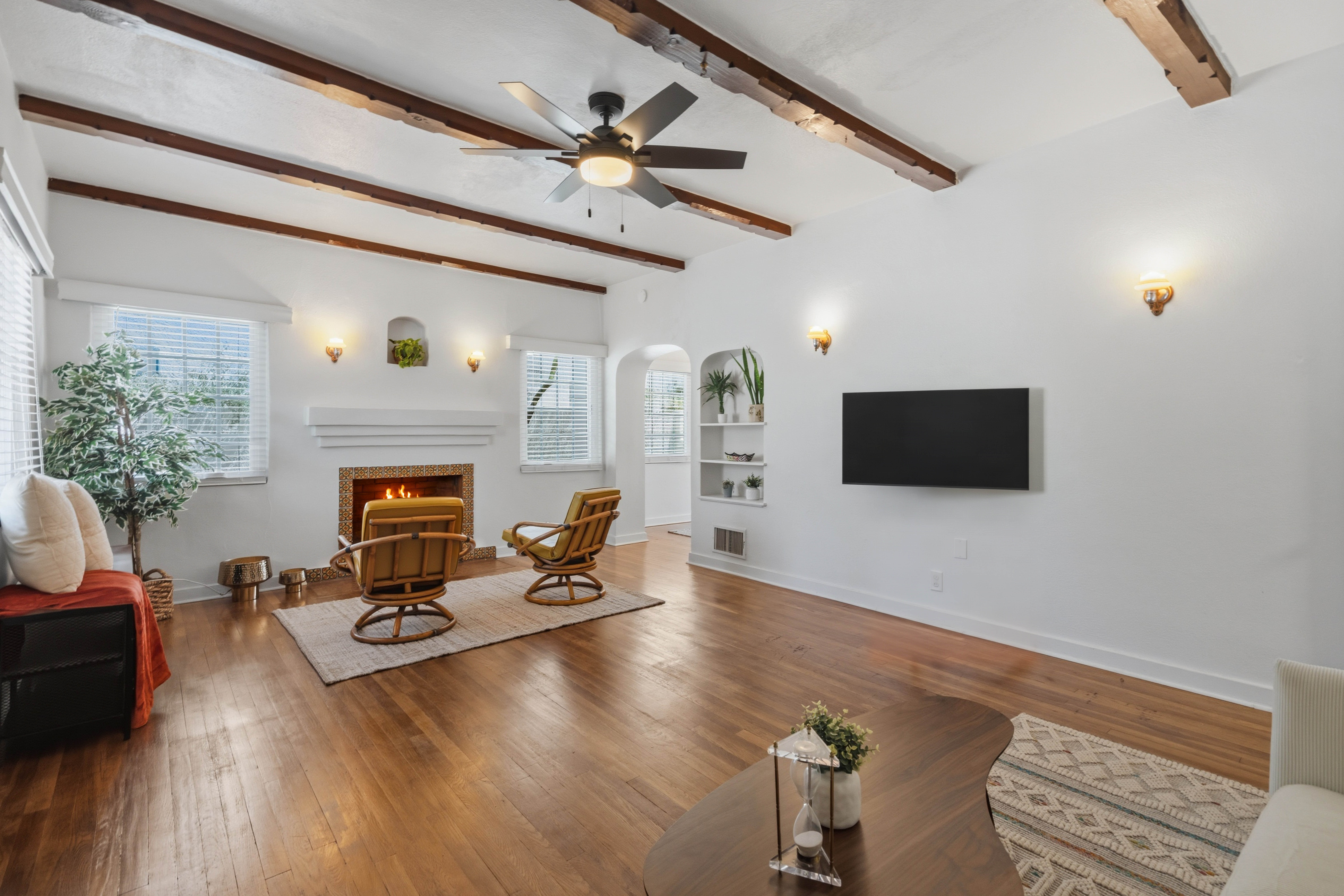 Bright living room with wood floors, exposed ceiling beams, and a fireplace.