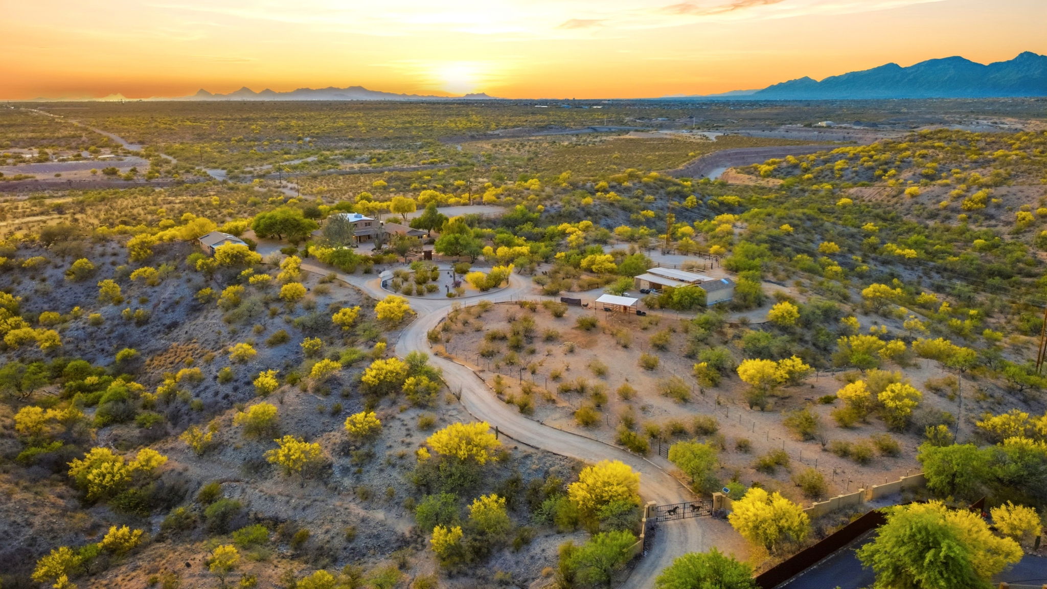 Wide aerial view of a desert property beneath an orange sunset