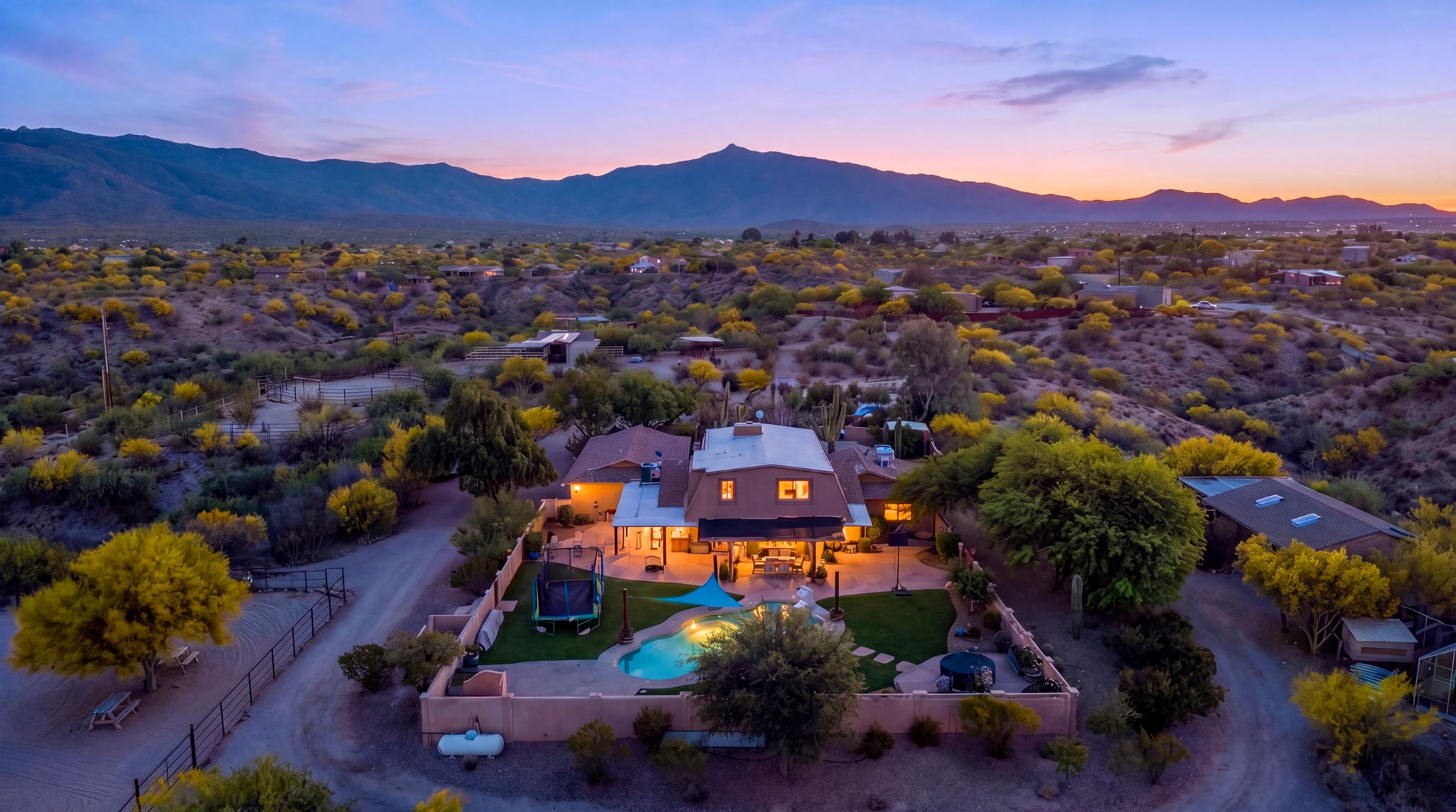 Aerial view of a ranch home and illuminated pool at dusk
