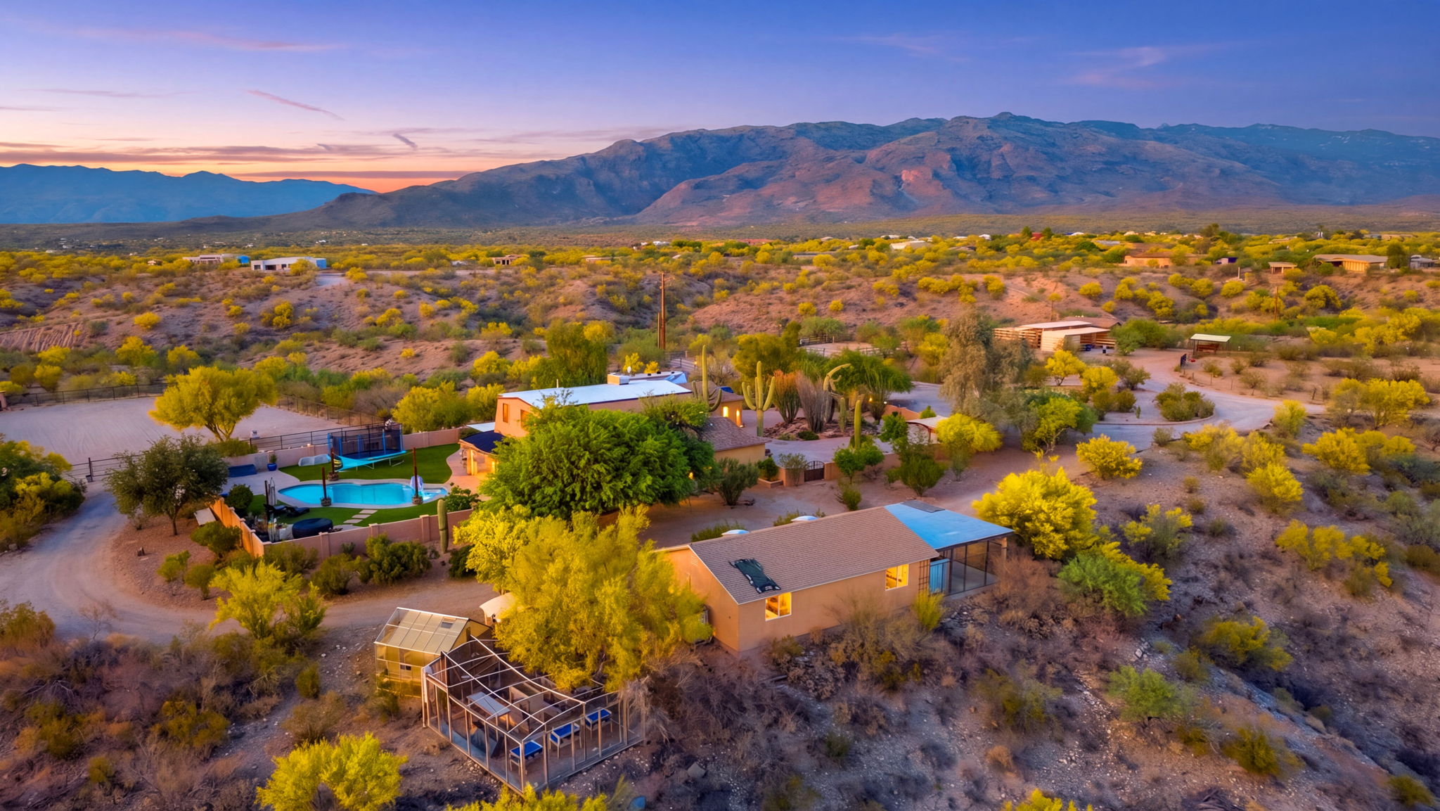 Wide aerial view of a ranch property and mountains at sunset