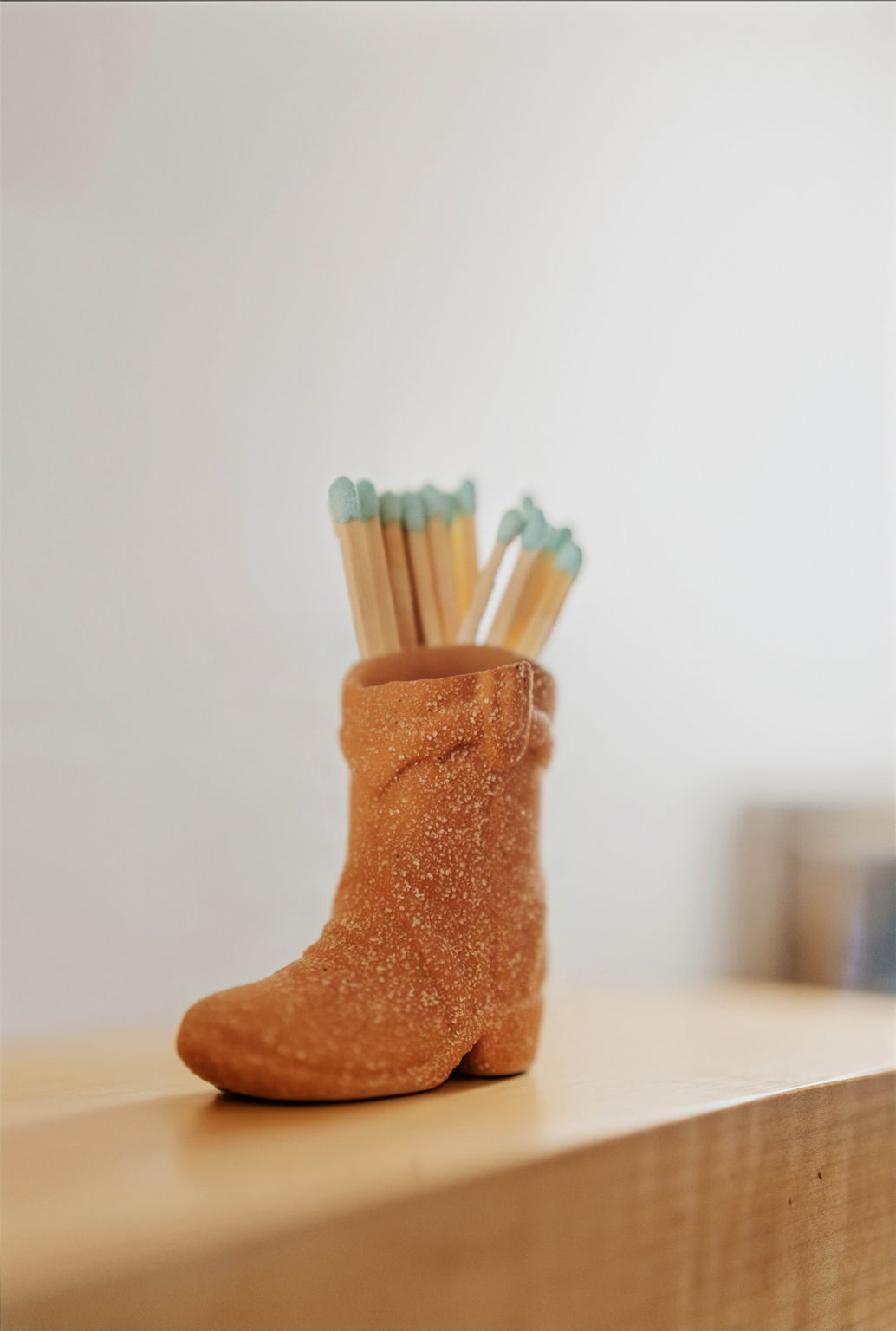 Terracotta cowboy boot match holder on a wooden shelf